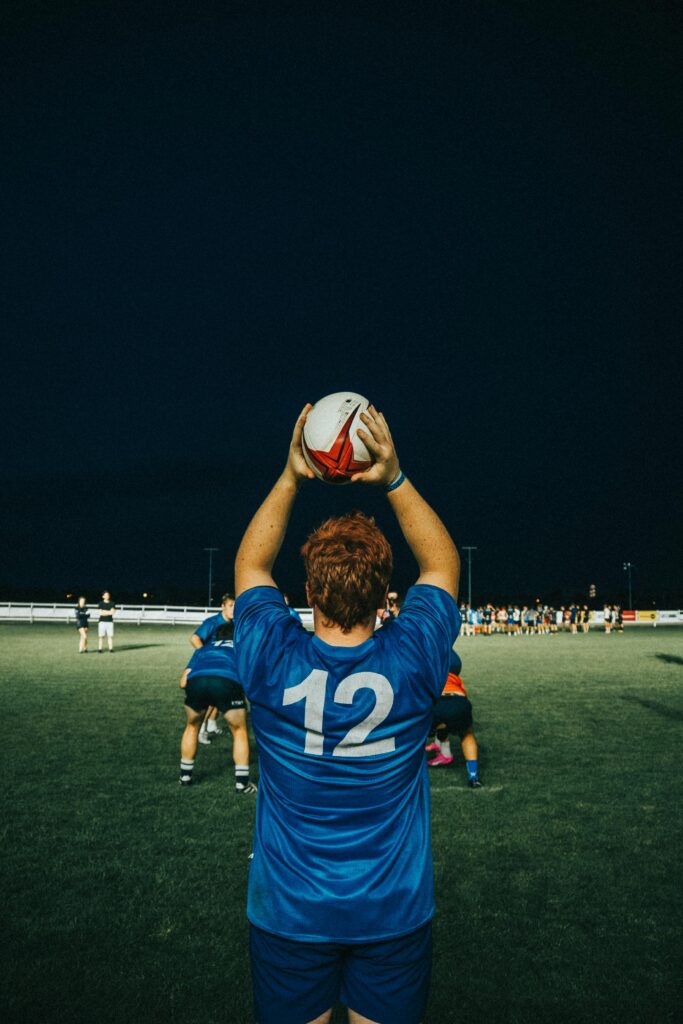 Rugby player in blue jersey preparing for lineout during a night game on an outdoor field.